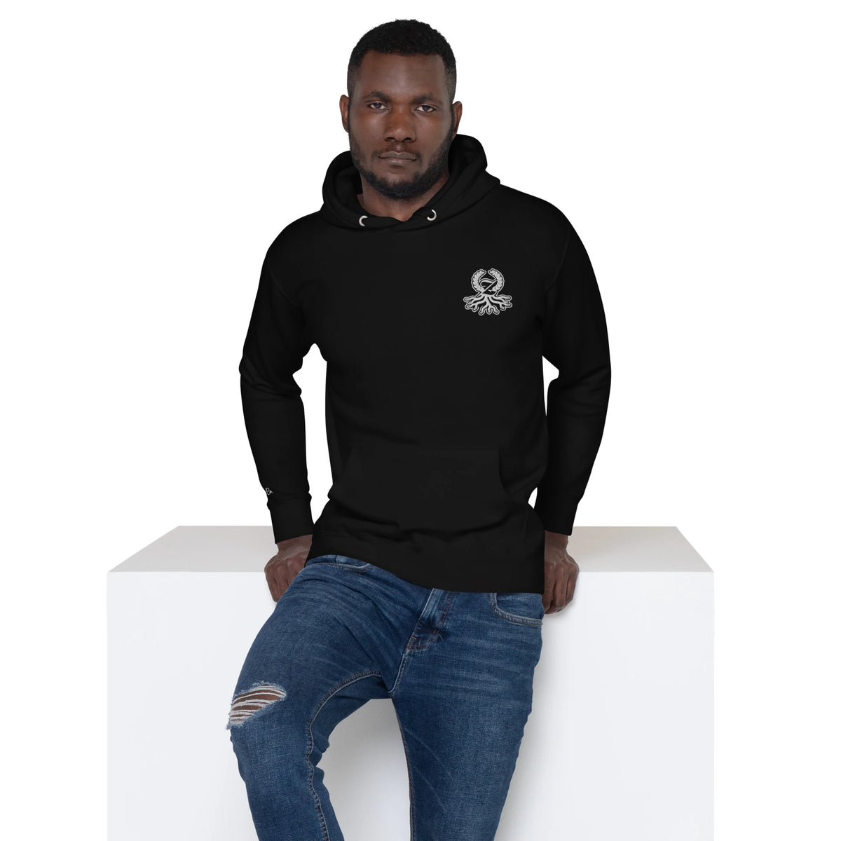 Hombre con sudadera premium negra Zaylachi Co. 288gsm sentado. Cara exterior 100% algodón streetwear unisex.